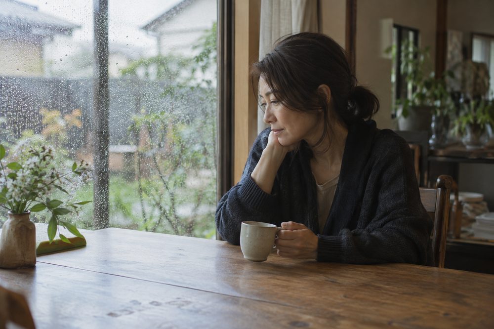 雨の日、窓辺でお茶を飲む女性