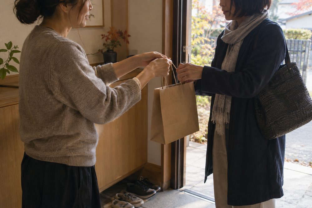 玄関で紙袋の手土産を手渡す様子